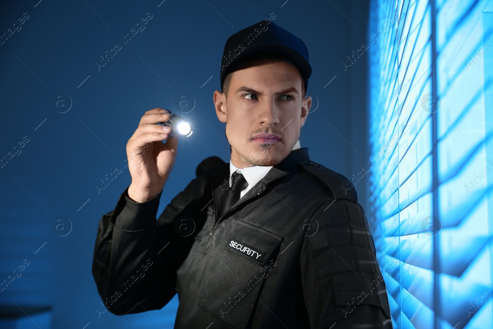 Photo of Professional security guard with flashlight near window in dark room