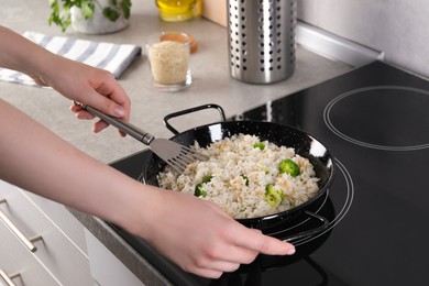 Photo of Woman frying rice with vegetables at induction stove in kitchen, closeup