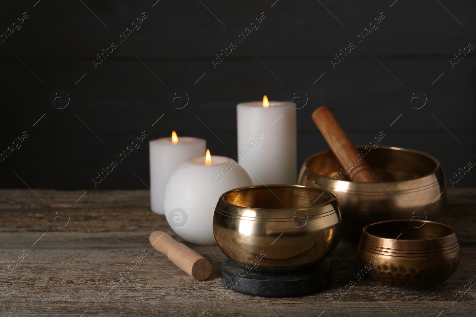 Photo of Golden singing bowls, mallets and burning candles on wooden table, space for text