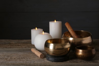 Photo of Golden singing bowls, mallets and burning candles on wooden table, space for text