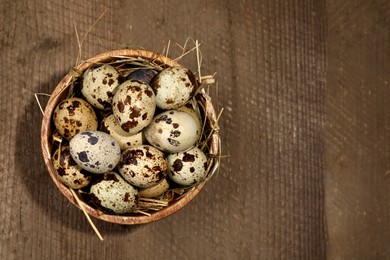 Photo of Bowl with quail eggs and straw on wooden table, top view. Space for text
