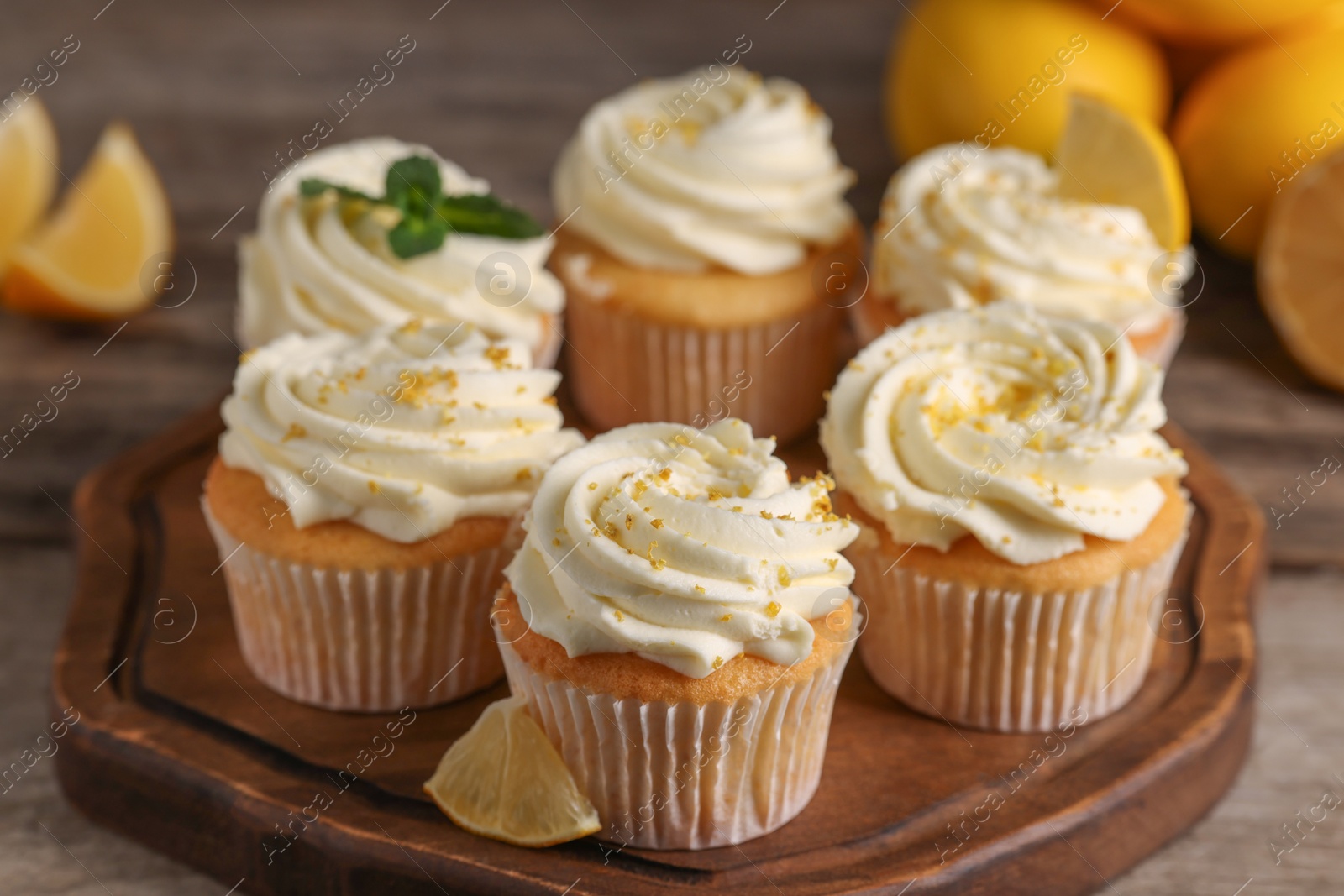 Photo of Delicious cupcakes with white cream and lemon zest on wooden table, closeup