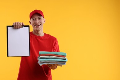 Dry-cleaning delivery. Happy courier holding folded clothes and clipboard on orange background, space for text