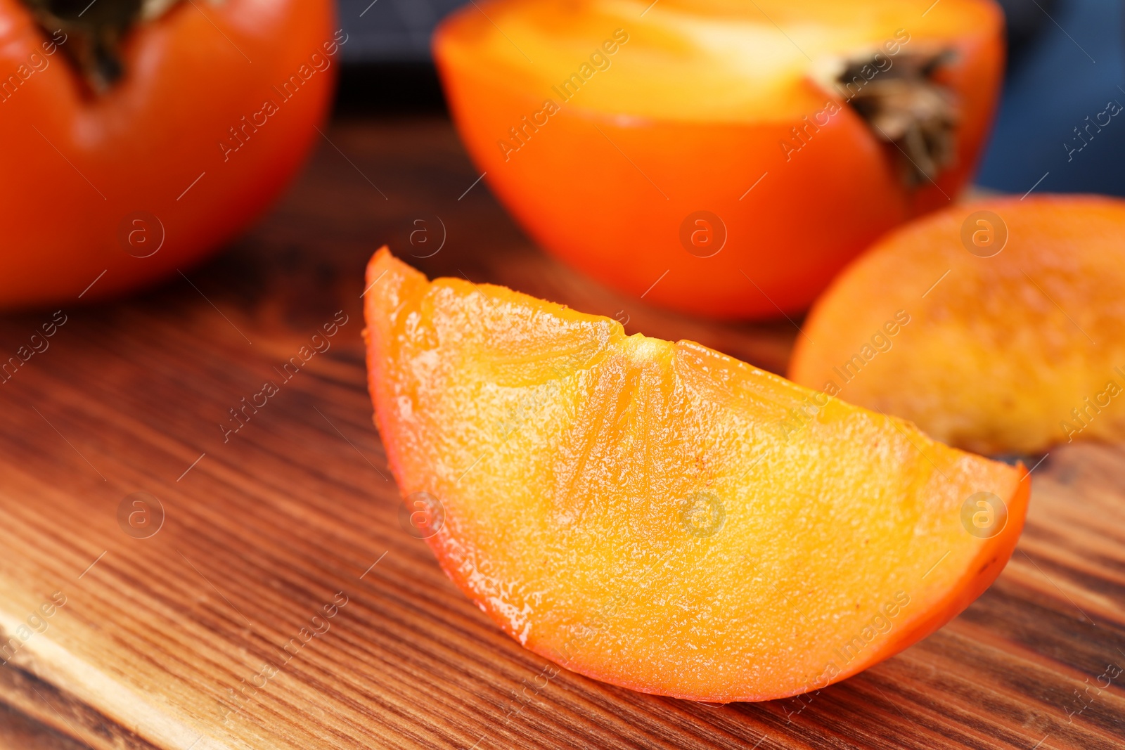 Photo of Piece of delicious ripe persimmon on wooden board, closeup