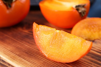 Photo of Piece of delicious ripe persimmon on wooden board, closeup