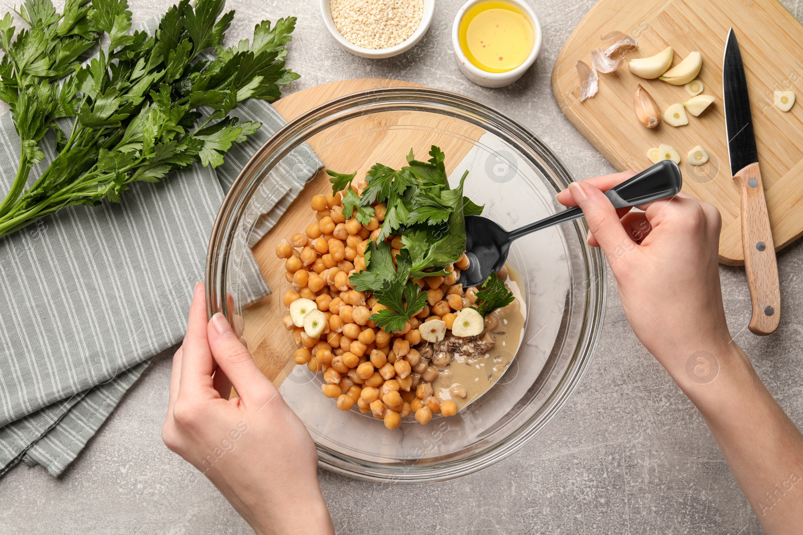 Photo of Woman mixing ingredients for delicious hummus at light grey table, top view