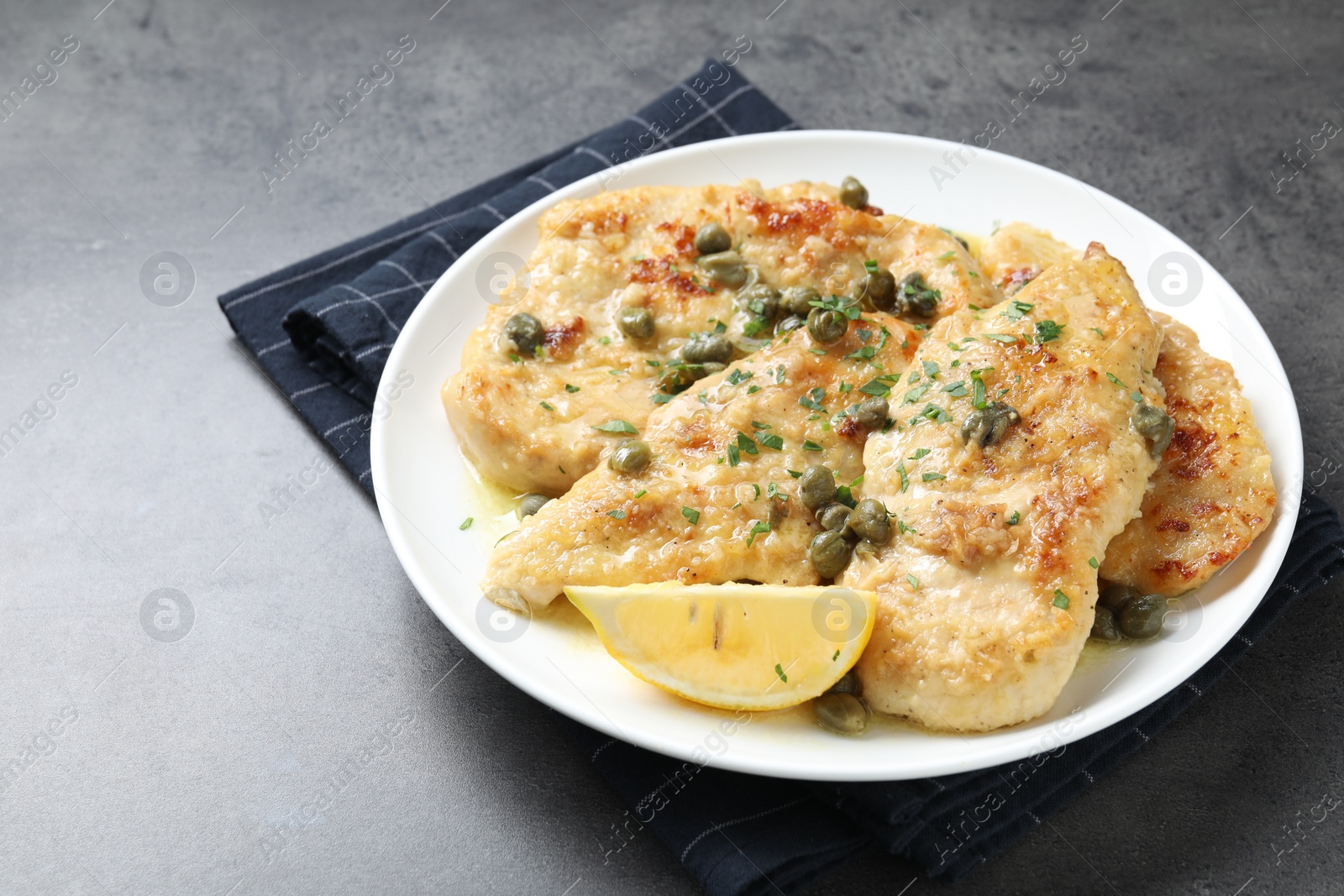 Photo of Delicious chicken piccata with herbs on grey table. Space for text