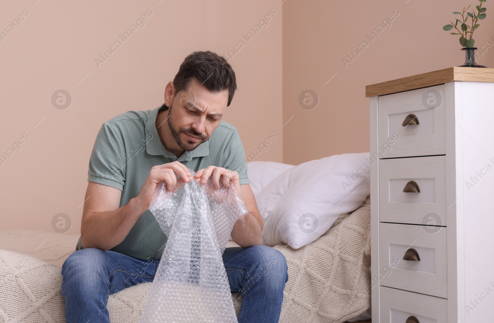 Photo of Man popping bubble wrap in bedroom at home. Stress relief