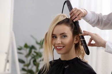 Photo of Hair styling. Hairdresser curling woman's hair in salon, closeup. Space for text