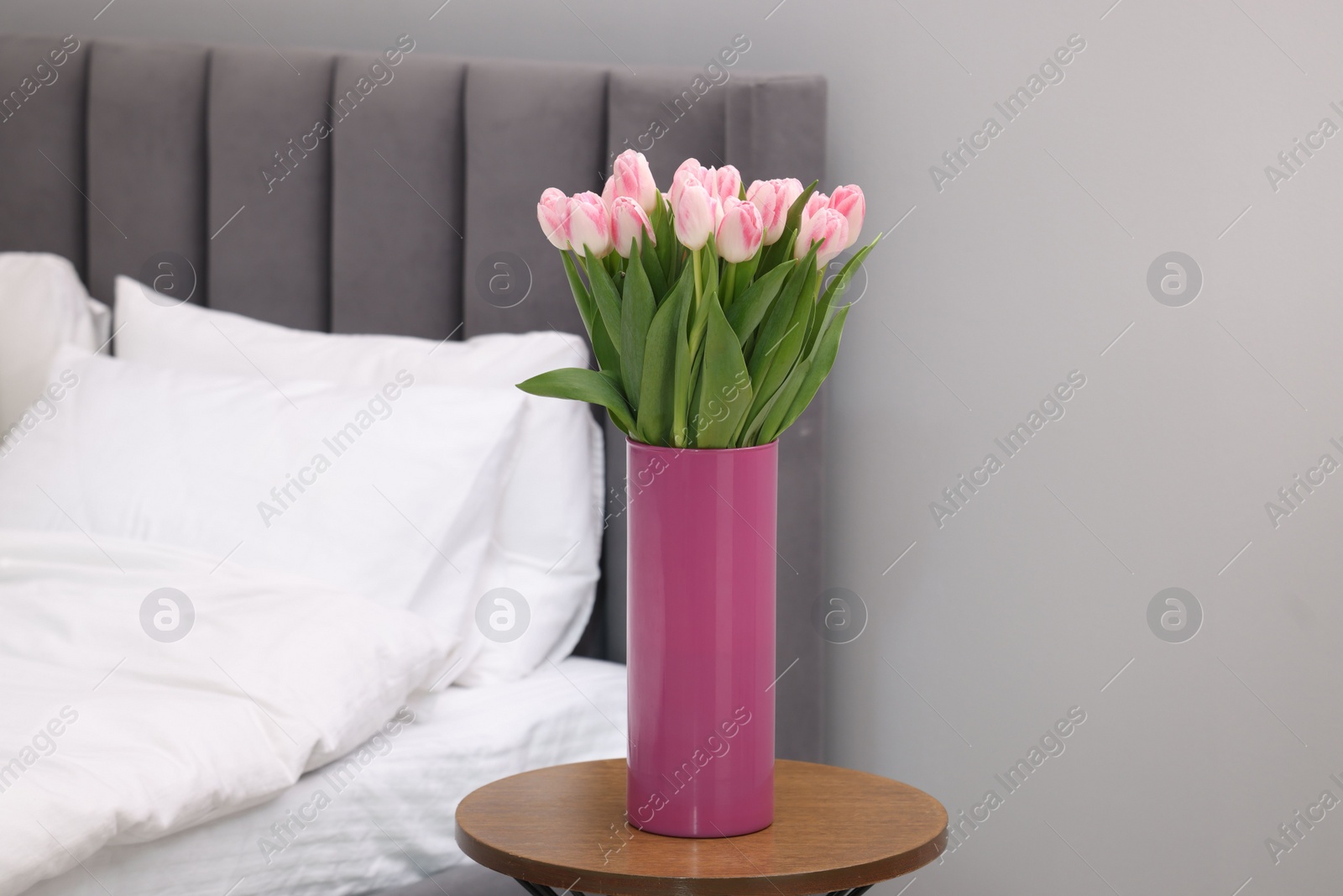 Photo of Beautiful bouquet of fresh pink tulips on bedside table in bedroom