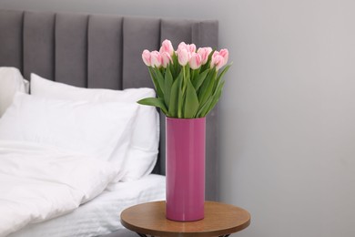 Beautiful bouquet of fresh pink tulips on bedside table in bedroom