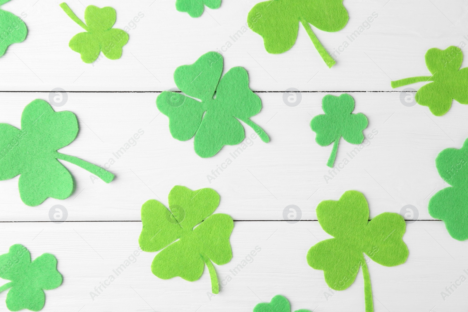 Photo of St. Patrick's day. Decorative green clover leaves on white wooden table, flat lay