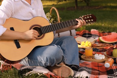 Photo of Young woman with guitar on plaid in park, closeup. Summer picnic
