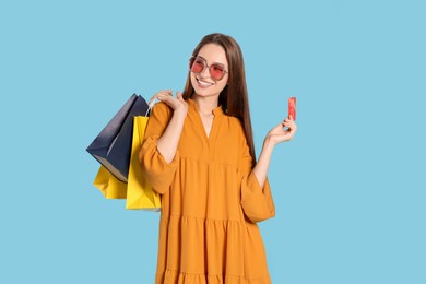 Photo of Happy young woman with shopping bags and credit card on light blue background. Big sale