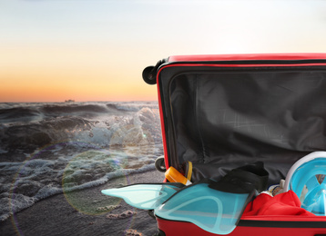 Image of Suitcase with different beach objects near sea at sunset, closeup. Space for text