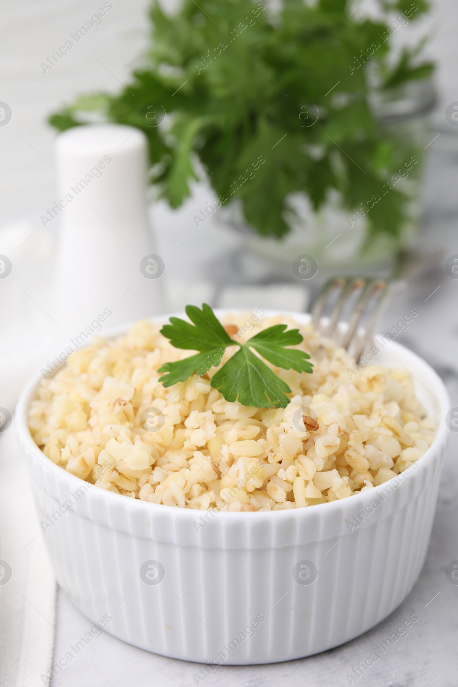 Photo of Cooked bulgur with parsley in bowl on white marble table, closeup