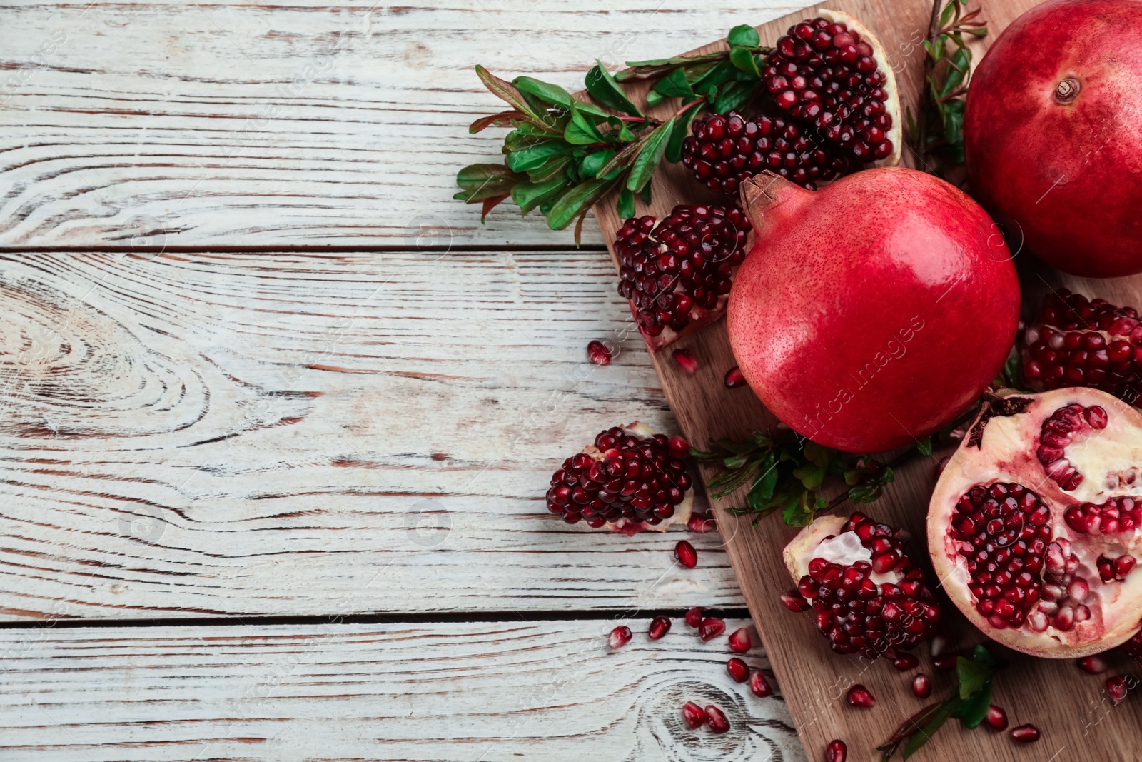 Photo of Delicious ripe pomegranates on white wooden table, flat lay. Space for text