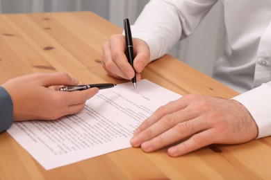 Businesspeople signing contract at wooden table in office, closeup of hands