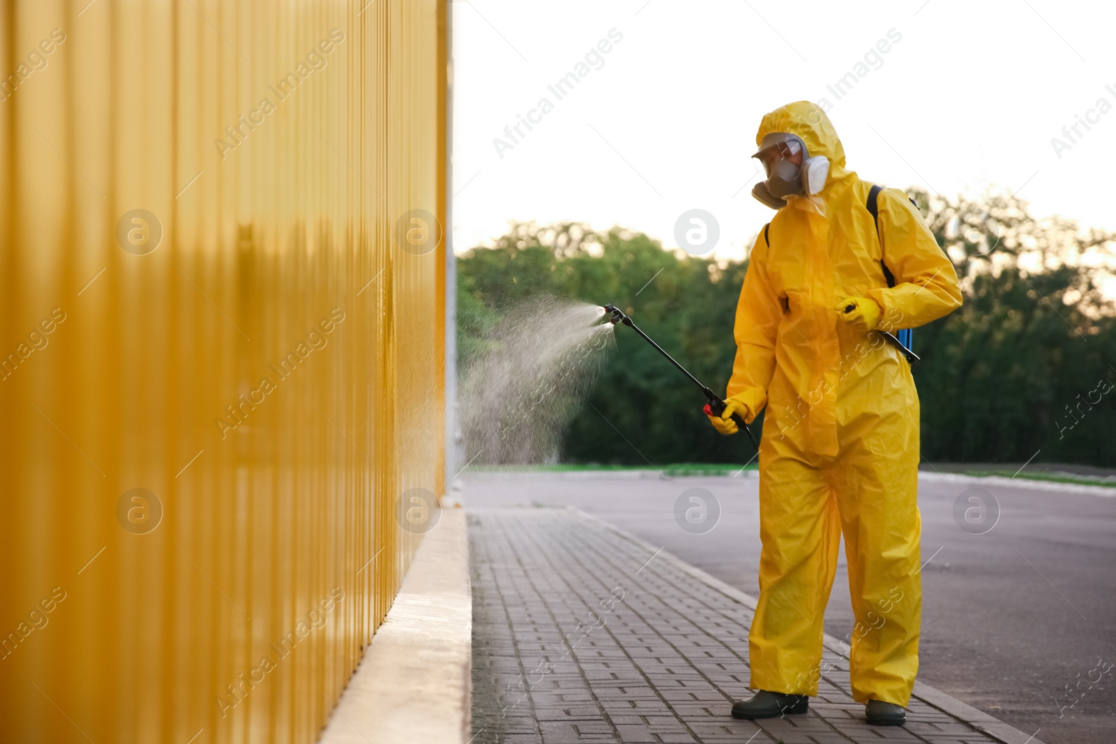 Photo of Person in hazmat suit disinfecting street with sprayer. Surface treatment during coronavirus pandemic