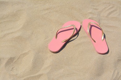 Photo of Stylish pink flip flops on sand, space for text