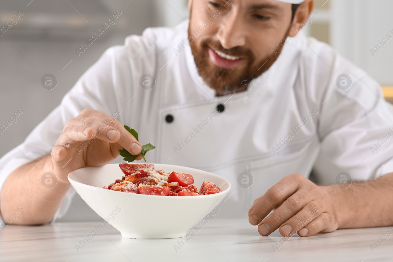 Photo of Professional chef decorating delicious spaghetti with parsley at marble table, focus on food