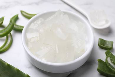 Photo of Aloe vera gel and slices of plant on white marble table, closeup