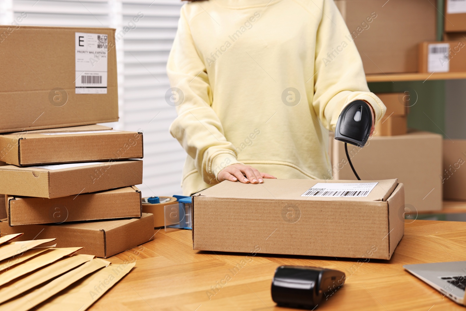 Photo of Parcel packing. Post office worker with scanner reading barcode indoors, closeup