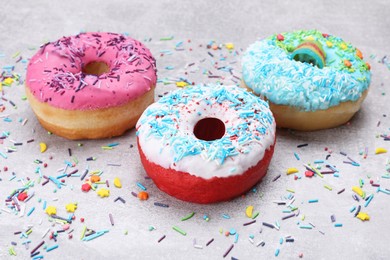 Sweet glazed donuts decorated with sprinkles on light grey table. Tasty confectionery