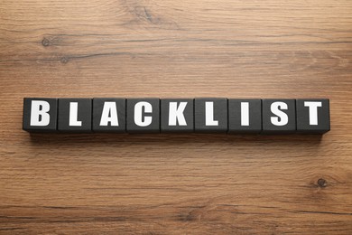Photo of Black cubes with word Blacklist on wooden background, flat lay