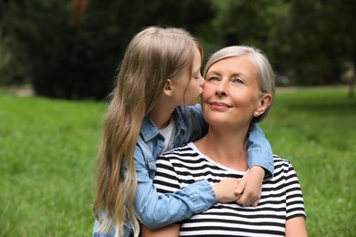 Photo of Happy granddaughter kissing her grandmother in park, space for text