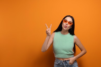 Photo of Beautiful young woman in stylish sunglasses blowing kiss on orange background. Space for text