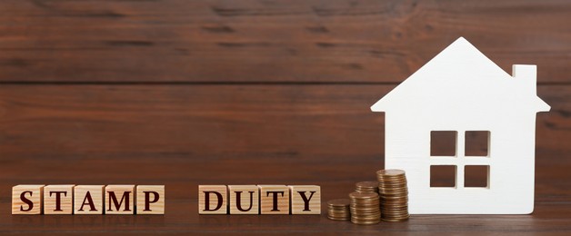 House model, cubes with text Stamp Duty and coins on wooden background. Banner design