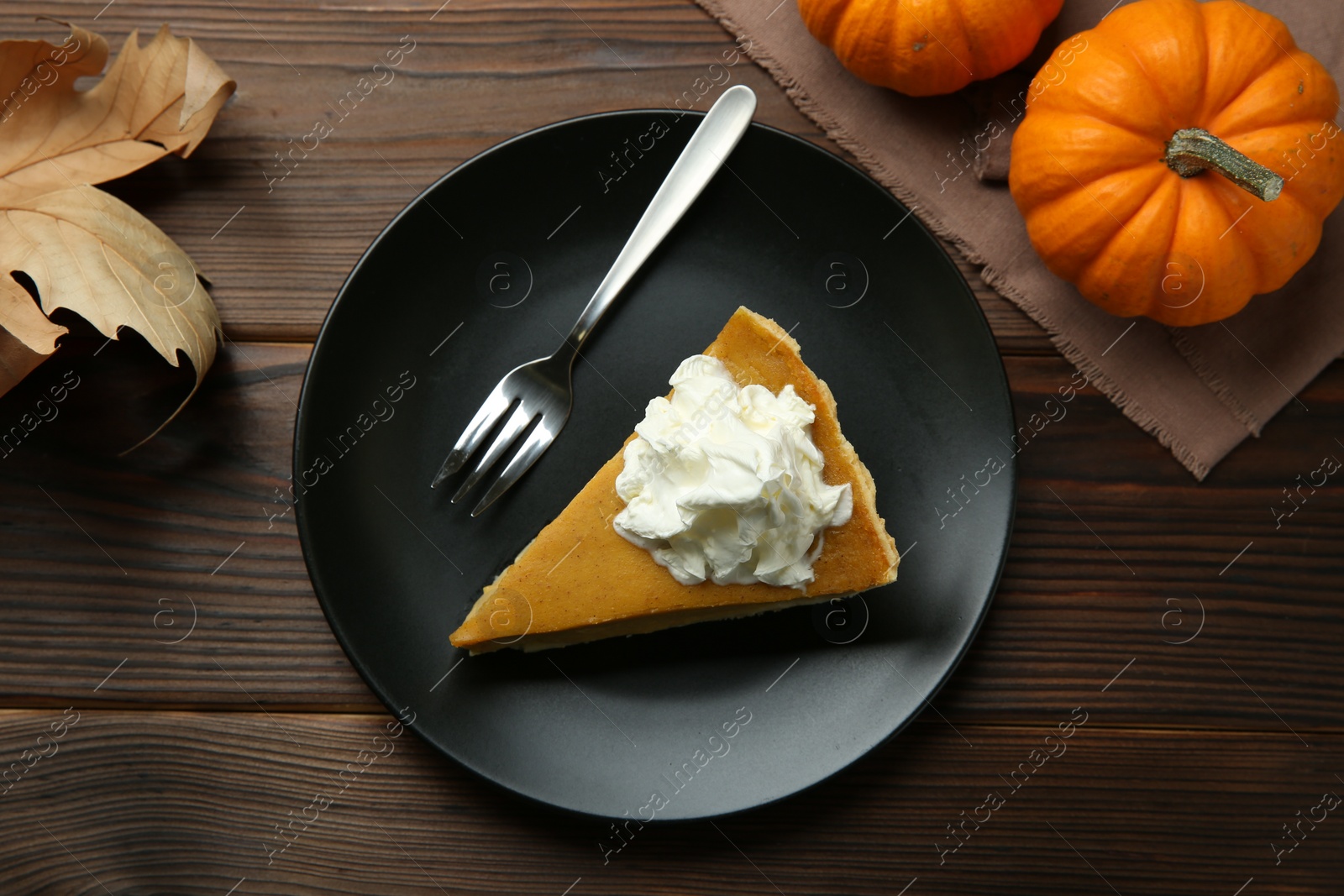 Photo of Piece of delicious pie with whipped cream, pumpkins and fork on wooden table, flat lay