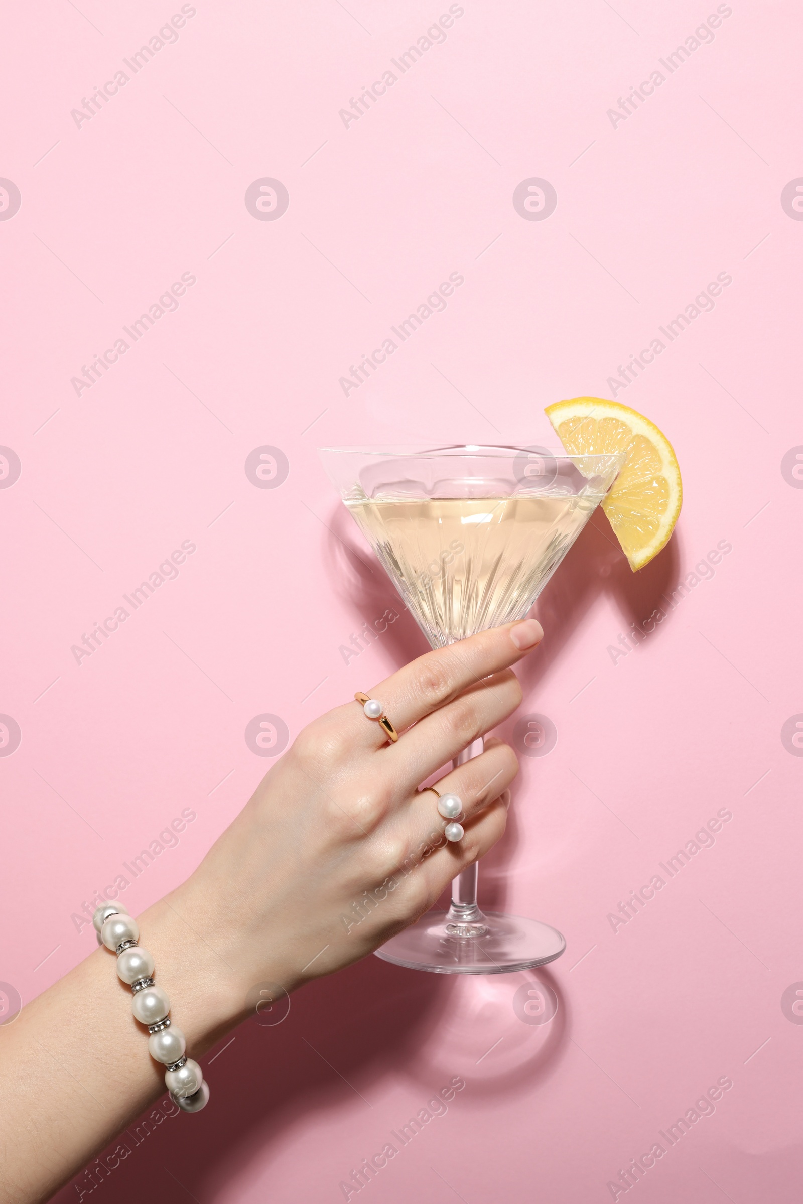 Photo of Woman holding martini glass of refreshing cocktail with lemon slice on pink background, closeup