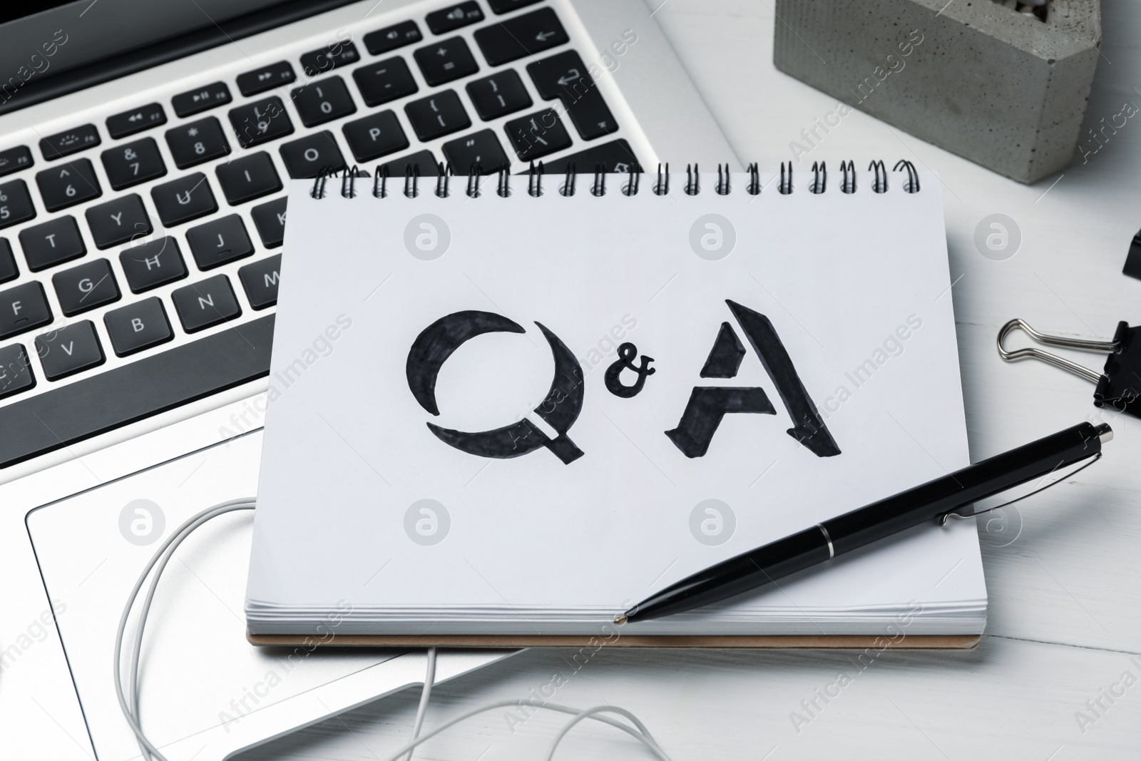 Photo of Notebook with text Q&A and laptop on white wooden table, closeup