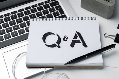 Notebook with text Q&A and laptop on white wooden table, closeup