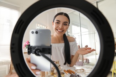 Photo of Beauty blogger recording video in dressing room at home, view through ring lamp