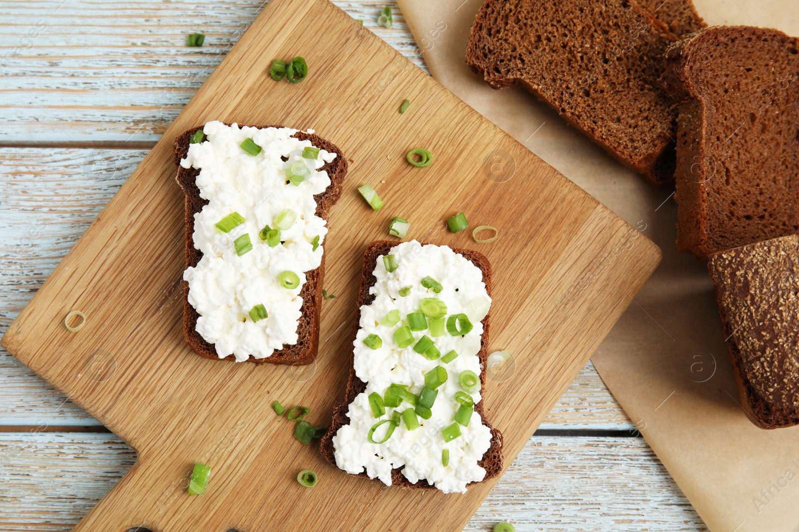 Photo of Bread with cottage cheese and green onion on light blue wooden table, flat lay