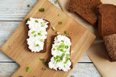 Photo of Bread with cottage cheese and green onion on light blue wooden table, flat lay