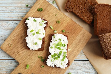 Bread with cottage cheese and green onion on light blue wooden table, flat lay