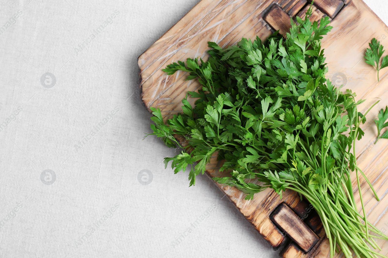 Photo of Wooden board with fresh green parsley and space for text on light fabric, top view