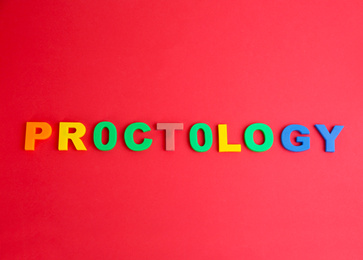 Photo of Word PROCTOLOGY made of colorful letters on red background, flat lay. Hemorrhoid problems