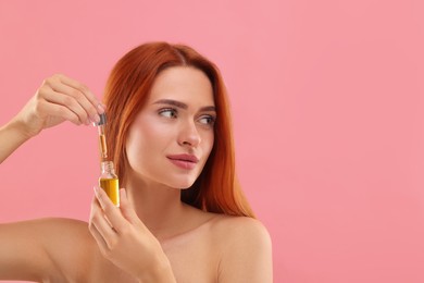 Photo of Beautiful young woman with bottle of cosmetic serum on pink background, space for text