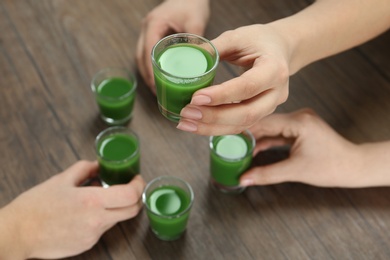 Photo of People with glasses of wheat grass juice at table, closeup