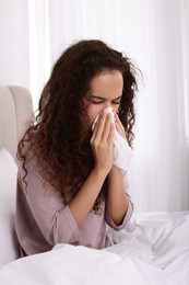 Sick African American woman with tissue in bed at home