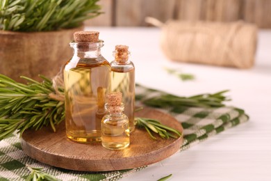 Photo of Essential oil in bottles and rosemary on white wooden table. Space for text