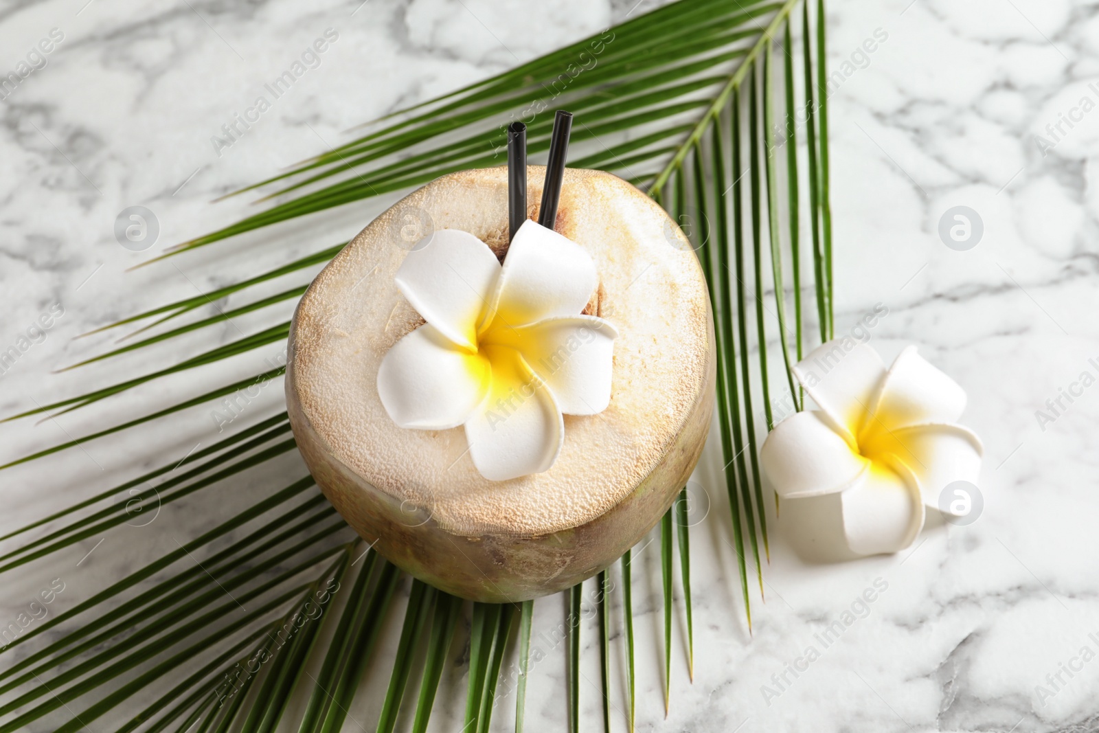 Photo of Fresh green coconut with flowers and palm leaf on table