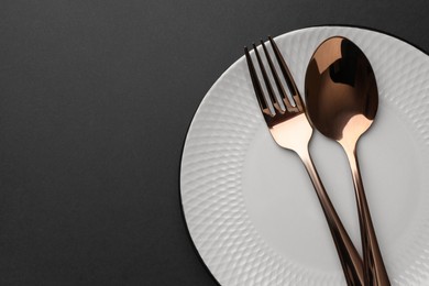 Photo of Clean plate and cutlery on black table, top view. Space for text