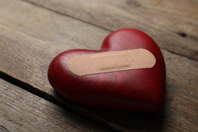 Photo of Heart with medical patch on wooden table, closeup. Relationship problems concept