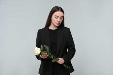 Photo of Sad woman with white rose flowers on light grey background. Funeral ceremony